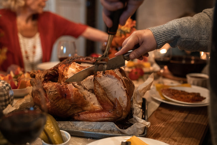 Family enjoying a turkey dinner while a man carves the turkey with a knife