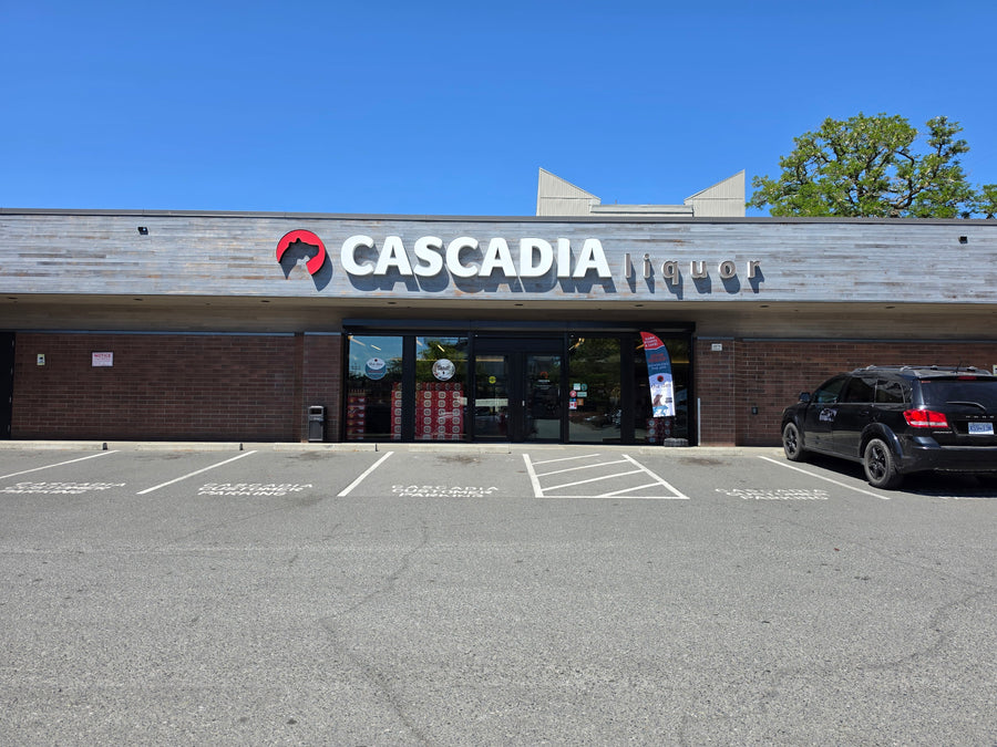Quadra Village Cascadia Liquor storefront with a sign indicating "Now Open!" and a parking lot in front.