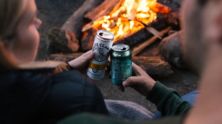 Couple enjoying cans of White Claw and Fat Tug by the campfire