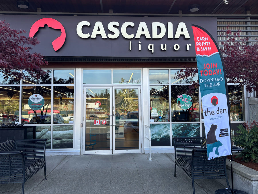 Storefront of Cascadia Liquor Courtenay with large signage and glass entrance, surrounded by greenery.